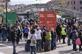caption: Stewards check tourists' QR code access outside the main train station in Venice, Italy, on Thursday.