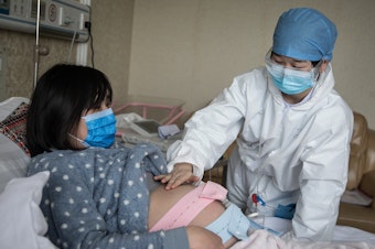 caption: A nurse examines a pregnant woman in a private obstetric hospital in Wuhan, Hubei Province, China, in February. Research from China suggests pregnancy does make women more vulnerable to the coronavirus.