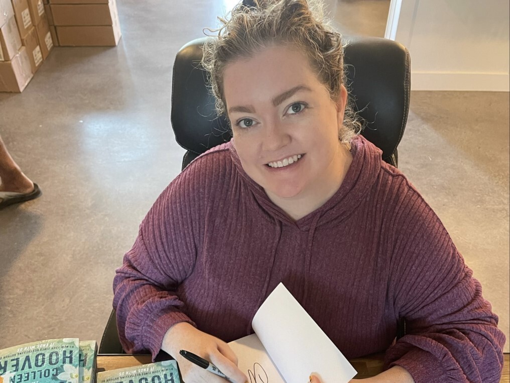 caption: Author Colleen Hoover signs her novel, "It Starts with Us."