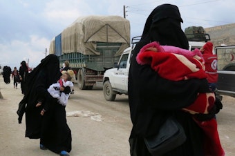 caption: Women carry children near the al-Hol camp in Syria's Kurdish-majority region of Rojava. The camp is filled with more than 72,000 people — most of them women and children who came out of the last ISIS-held territory.