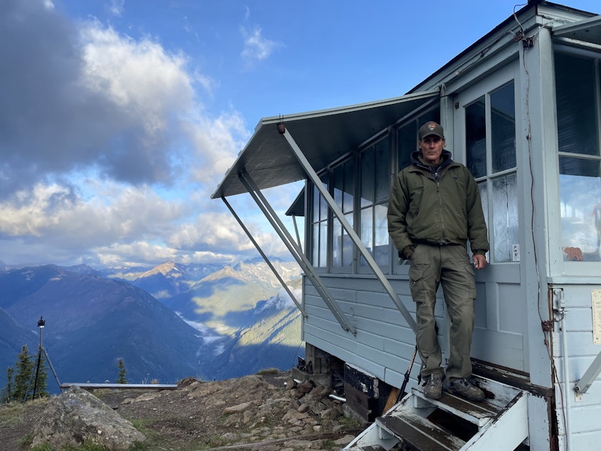caption: Jim Henterly poses outside the door of the Desolation Peak Fire Lookout in the North Cascades Wilderness. 