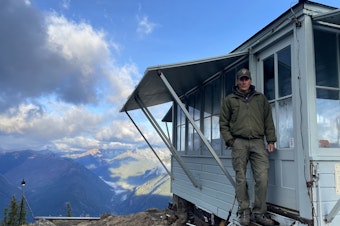 caption: Jim Henterly poses outside the door of the Desolation Peak Fire Lookout in the North Cascades Wilderness. 