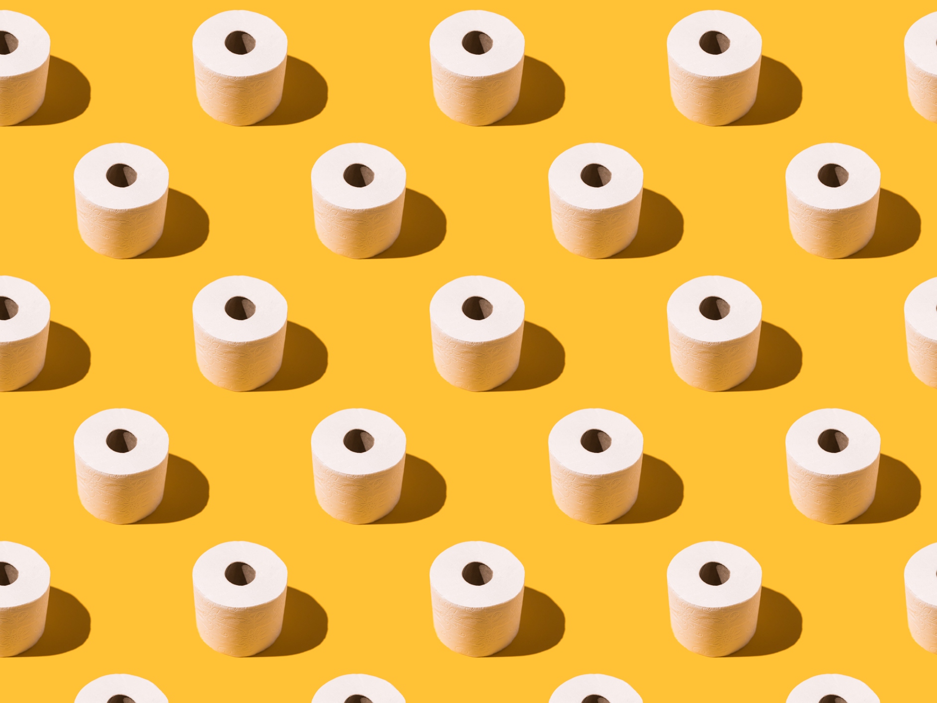 Pattern of white toilet paper rolls on yellow background. Concept of going to the bathroom, cleaning and pooping and peeing.