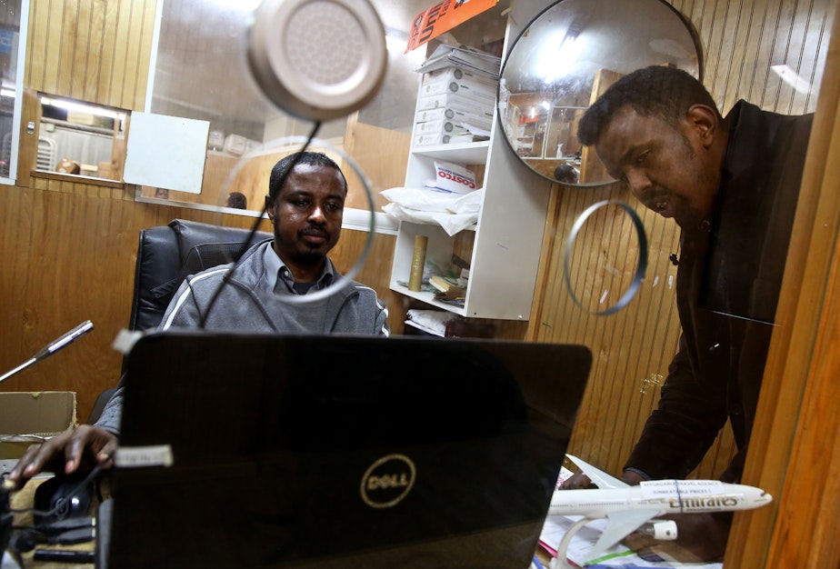 caption: Adem Issa, an employee at Tawakal Express CQ, works on a money transfer for Mohmed Egal in SeaTac, Wash. Egal was sending money to Nairobi, Kenya, to help with his brother's education.