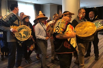 caption: Representatives of Washington tribes perform a "paddle song" at the start of a 2018 hearing in Victoria, B.C., to oppose the Trans Mountain Pipeline