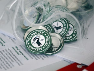 caption: Pro-union pins sit on a table during a watch party for Starbucks' employees union election, Dec. 9, 2021, in Buffalo, N.Y. The top lawyer for the National Labor Relations Board said Thursday, April 7, she will ask the board to rule that mandatory meetings some companies hold to persuade their workers reject unions is in violation of federal labor law.
