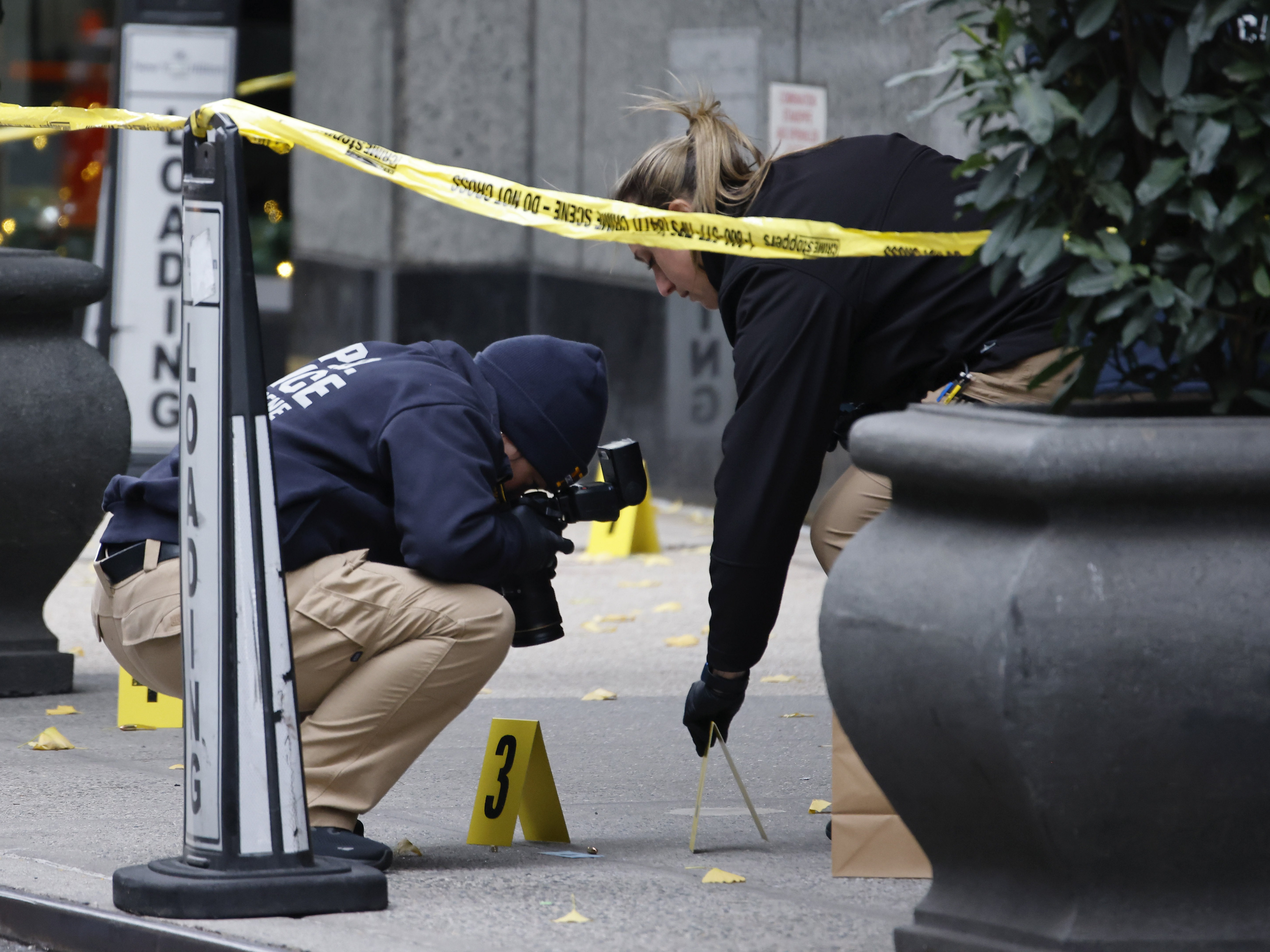 caption: Members of the New York police crime scene unit photograph bullets lying on the sidewalk as they investigate the scene outside the Hilton Hotel in midtown Manhattan where Brian Thompson was fatally shot on Wednesday.