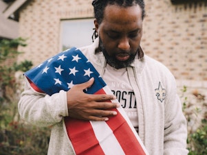 caption: Edmund Garcia, an Iraq war veteran, holds the American flag over his shoulder outside his home on Thursday in Rosharon, Texas.