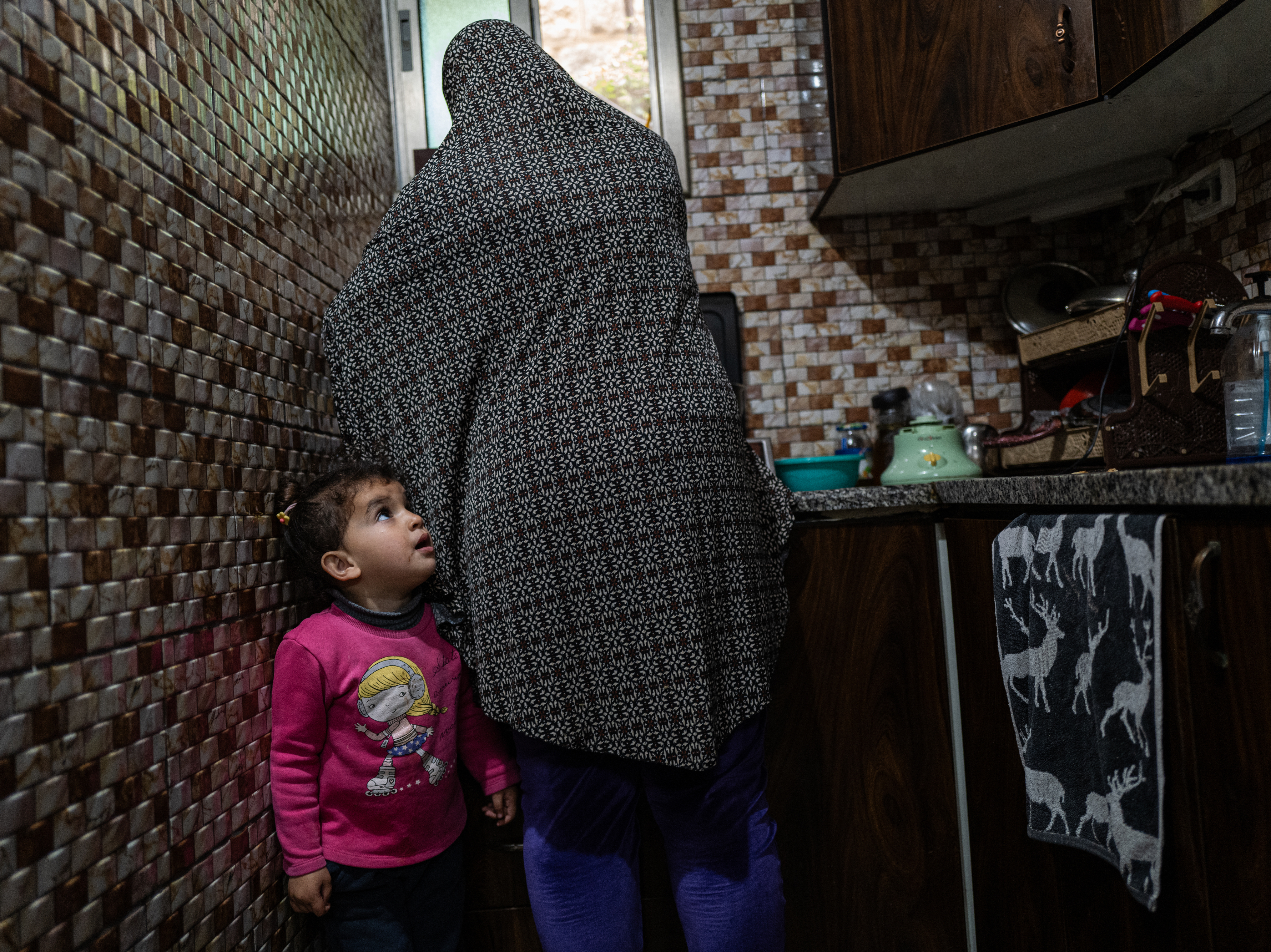 caption: Sally Zeita, 3, stands beside her mother Amani as she prepares a Ramadan dessert at their home in the village Ein 'Arik in the occupied West Bank on March 24.