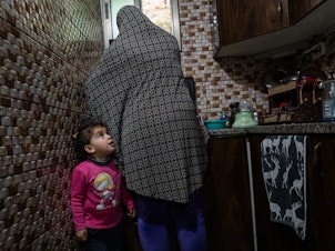 caption: Sally Zeita, 3, stands beside her mother Amani as she prepares a Ramadan dessert at their home in the village Ein 'Arik in the occupied West Bank on March 24.