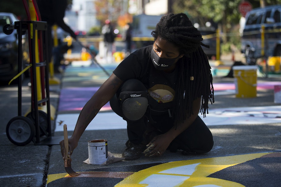 caption: Aramis O. Hamer paints the letter V in the Black Lives Matter street mural on Friday, October 2, 2020, on E. Pine Street in Seattle. 