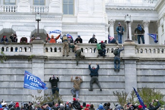 caption: In this Jan. 6, 2021 file photo rioting supporters of President Donald Trump climb the west wall of the the U.S. Capitol in Washington. Historians say Trump’s legacy and his electoral undoing will be largely shaped by rhetoric aimed at stirring his largely white base that tugged at the long-frayed strands of race relations in America. 