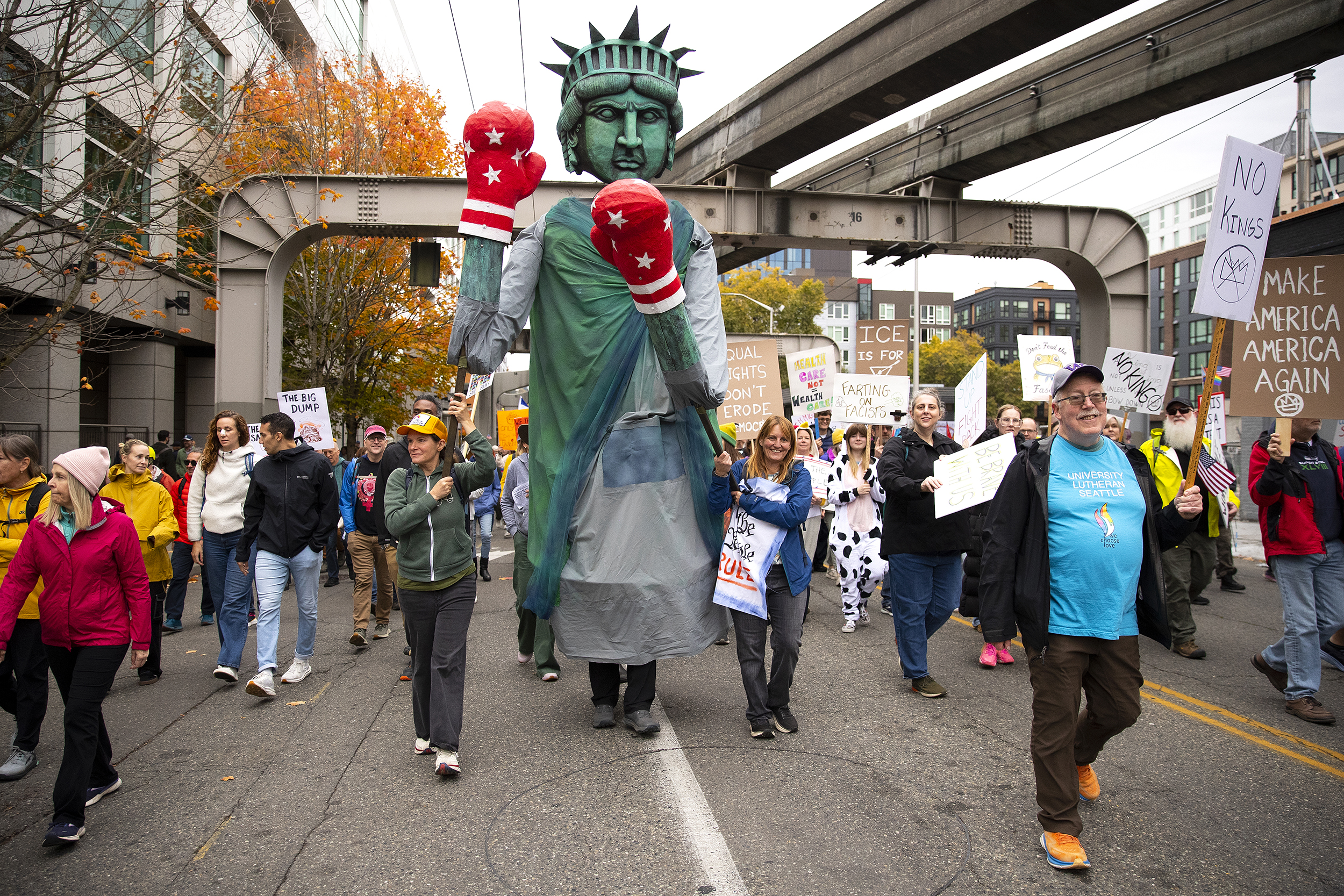 caption: Protesters guide a large Lady Liberty wearing boxing gloves while marching following the No Kings rally on Saturday, October 18, 2025, outside of Seattle Center. 