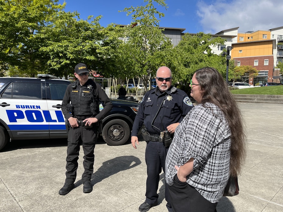 caption: Burien Police Officer Mark Hayden, center, asks Cydney Moore, right, to inform homeless campers about trash pickups and upcoming street fairs in downtown Burien. 