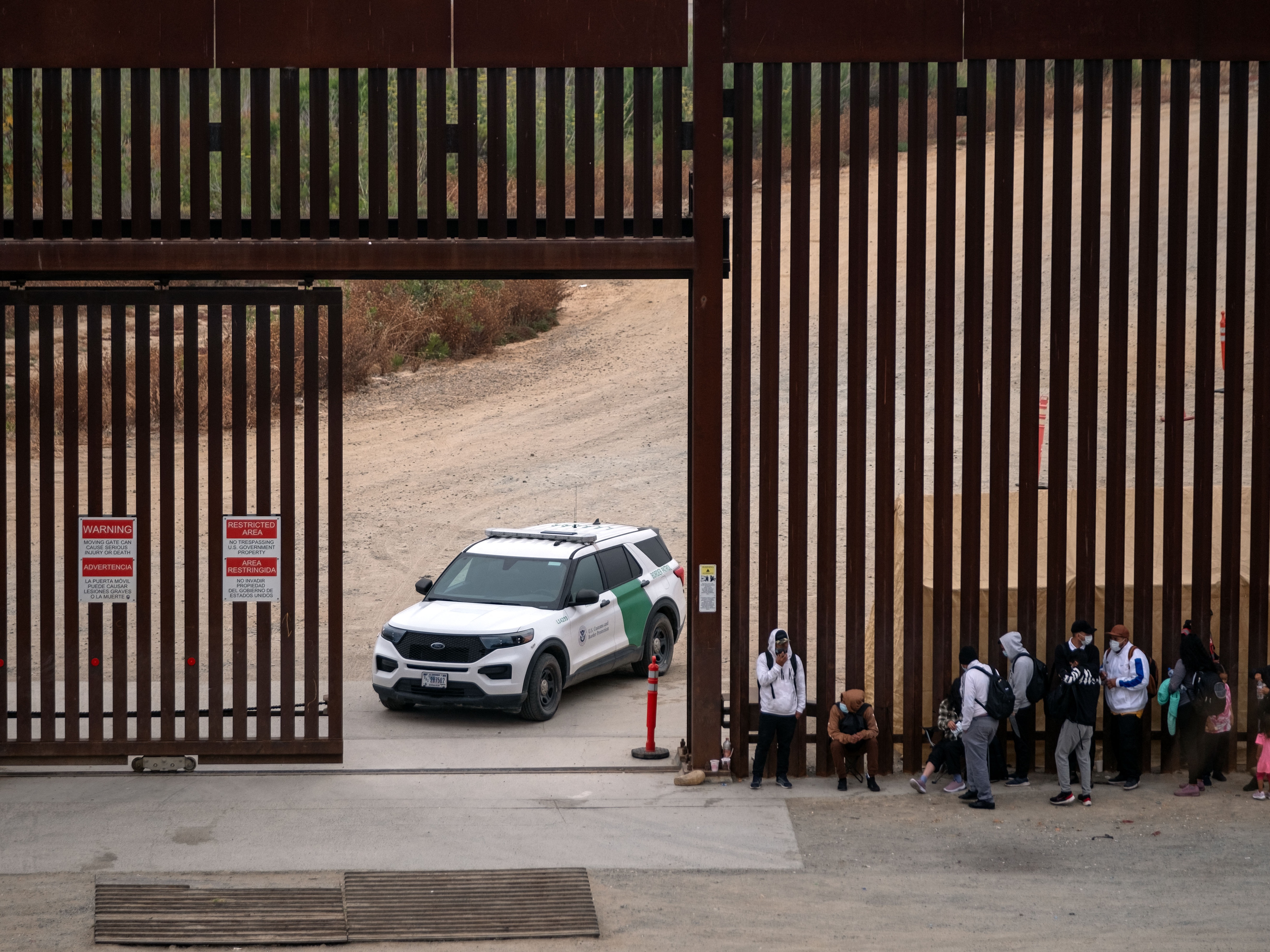 caption: Migrants and asylum seekers wait to be processed by the Border Patrol between the fence at the US-Mexico border seen from Tijuana, Baja California state, Mexico, on June 5, 2024, the day after President Joe Biden issued executive actions that restrict asylum for most migrants.
