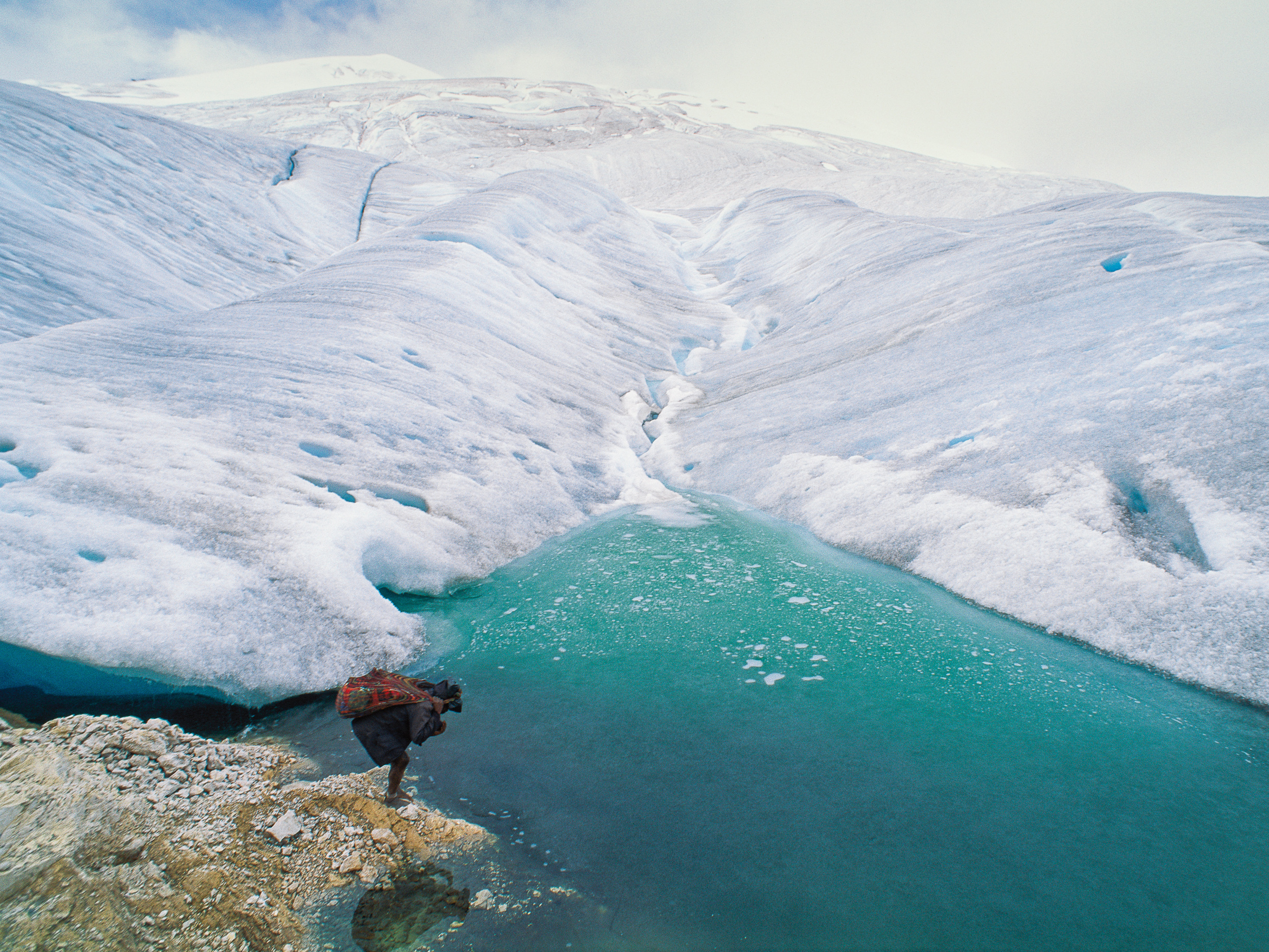 caption: A barefoot porter totes a load for an expedition visiting one of the remaining glaciers near the equator, 16,000 feet high on the highest peak in Papua, Indonesia.