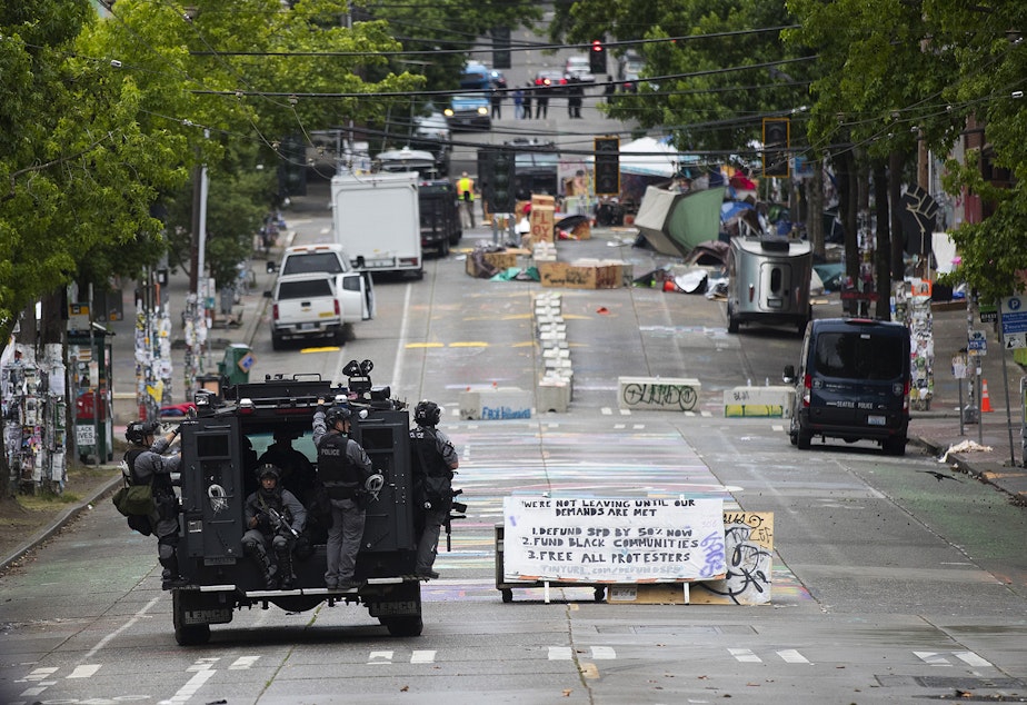 caption: Seattle Police Department officers drive an armored vehicle through the former Capitol Hill Organized Protest zone after the zone was cleared by Seattle Police Department officers early Wednesday morning, July 1, 2020, in Seattle.