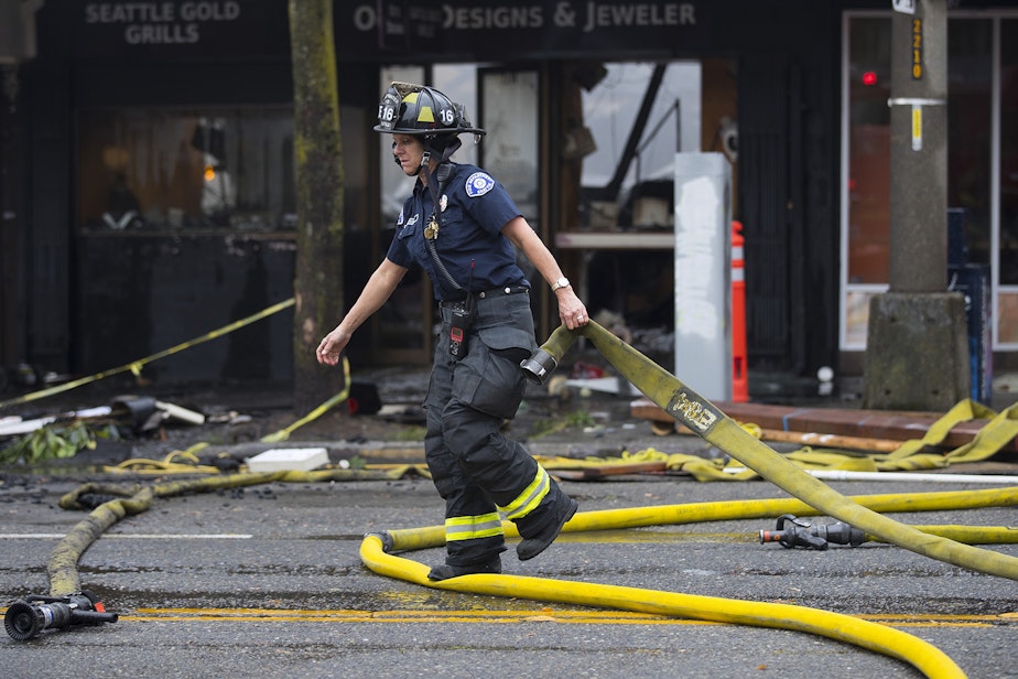 caption: Firefighters work to put out a fire on Monday, October 7, 2019, near the intersection of NW Market Street and 24th Avenue Northwest in Seattle.
