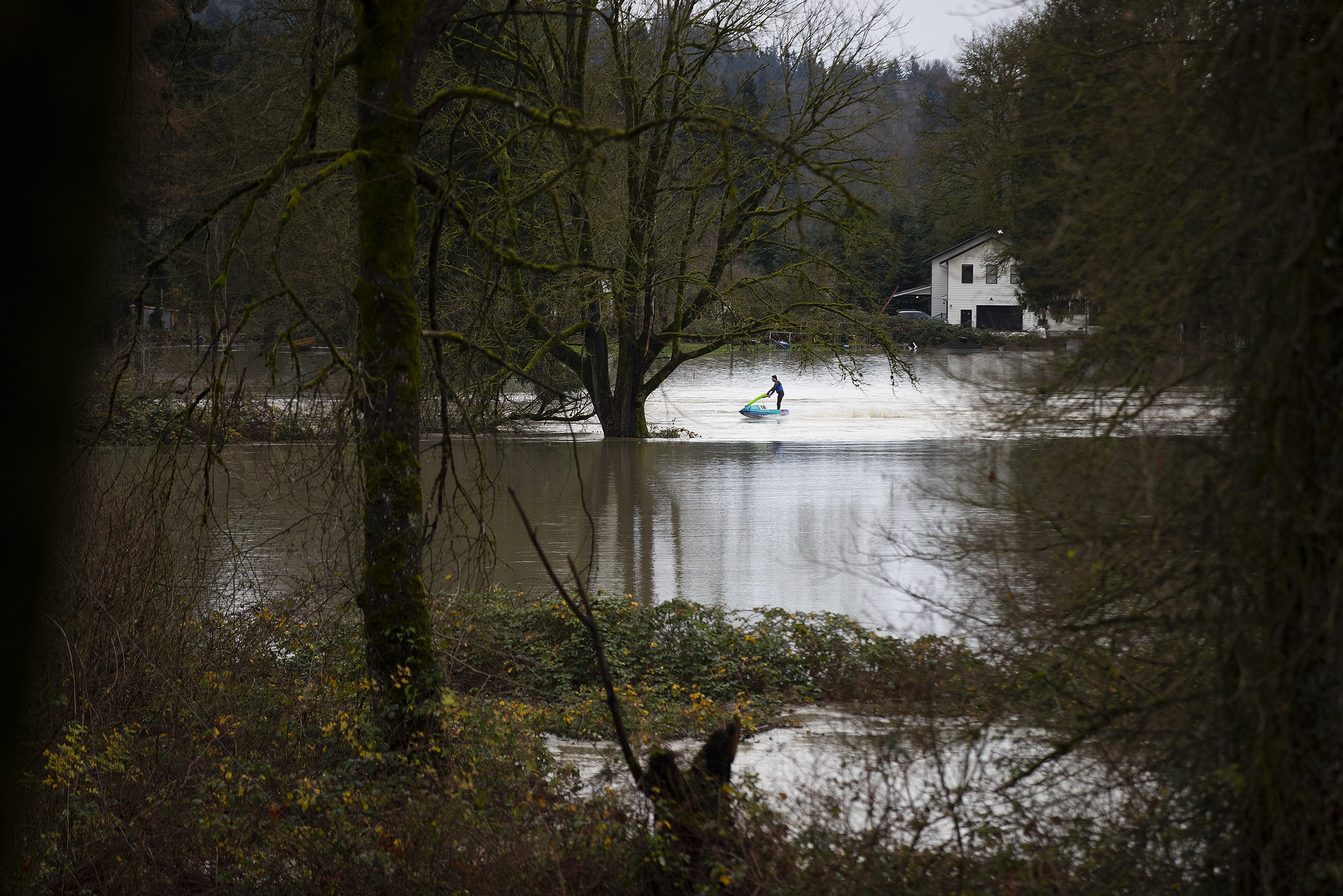 caption: A person jet skis through floodwaters near the Skykomish River on Thursday, December 11, 2025, in Monroe. 