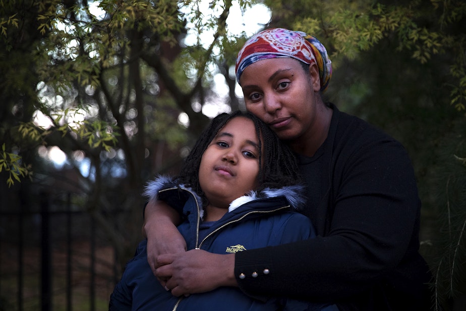 caption: Asmeret Habte hugs her 9-year-old daughter, Kisanet Yohannes, while standing for a portrait on Monday, November 29, 2021, outside of their home in Burien. Yohannes was a 4th-grade student at Impact Puget Sound Elementary before she unenrolled several months ago. 