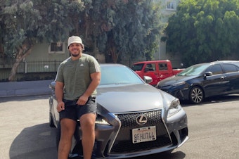 caption: Johnny Navarro sits on the hood of his recently purchased 2014 Lexus.