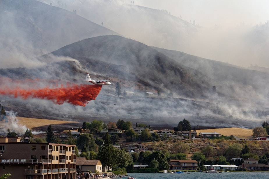 caption: A plane flies over Chelan within hours of a wildfire starting on Aug. 14, 2015. Sunbathers on holiday watched as the fire effort took hold. 