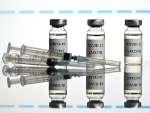 caption: An illustration picture shows vials with COVID-19 vaccine stickers attached and syringes with the logo of U.S. biotechnology company Moderna on November 17.