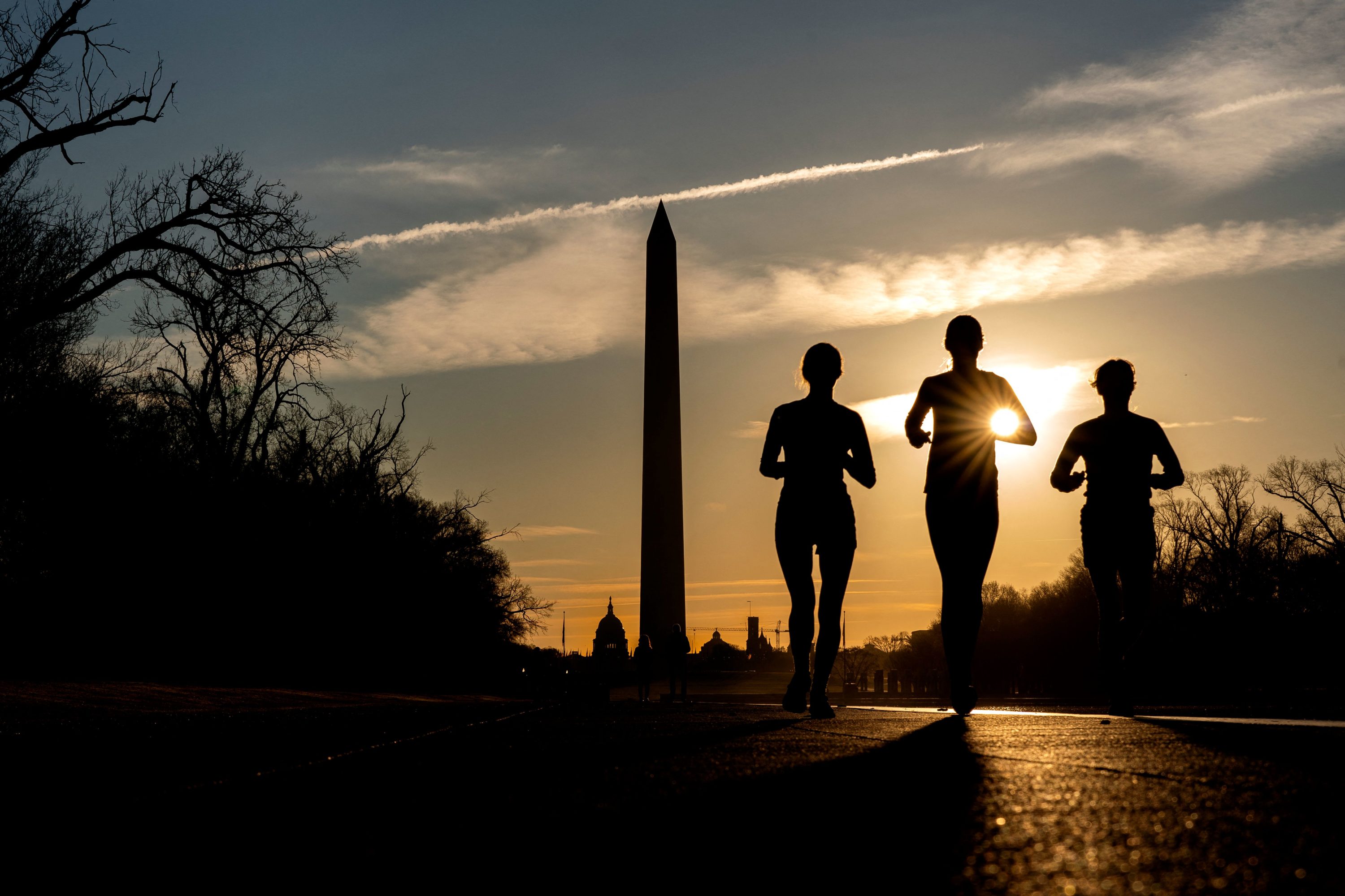 caption: People run along the National Mall at sunrise in Washington, DC, on March 15, 2022. (Stefani Reynolds/AFP via Getty Images)