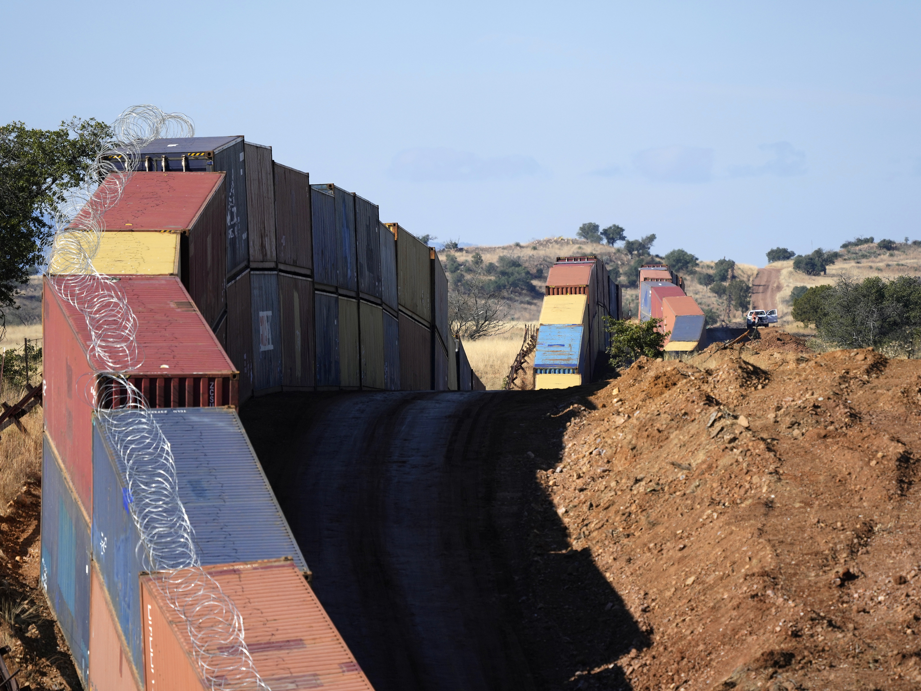 caption: A long row of double-stacked shipping containers provide a new wall between the United States and Mexico in the remote section of San Rafael Valley, Ariz., on Dec. 8, 2022.