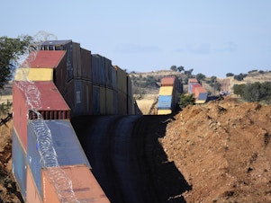 caption: A long row of double-stacked shipping containers provide a new wall between the United States and Mexico in the remote section of San Rafael Valley, Ariz., on Dec. 8, 2022.
