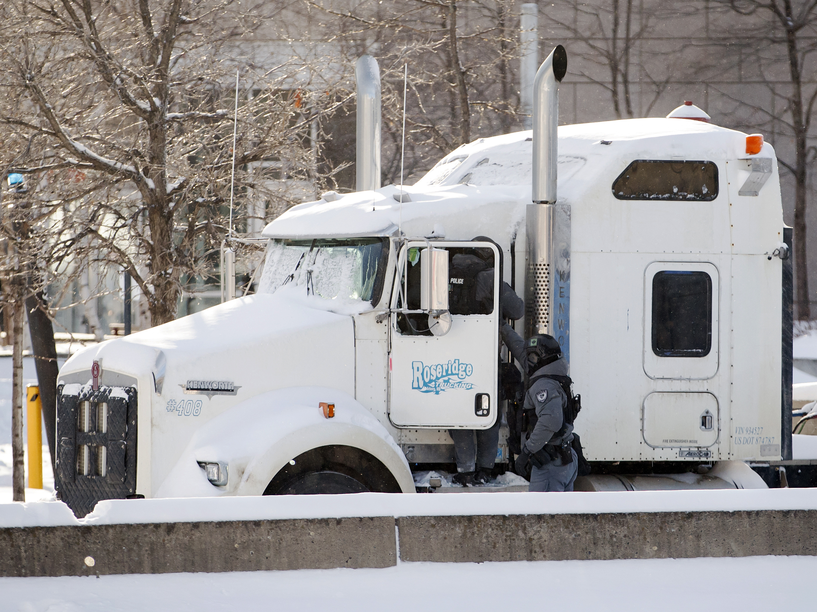 caption: Police officers enter a blockade protest truck parked in downtown Ottawa on Friday as they began arresting protesters.