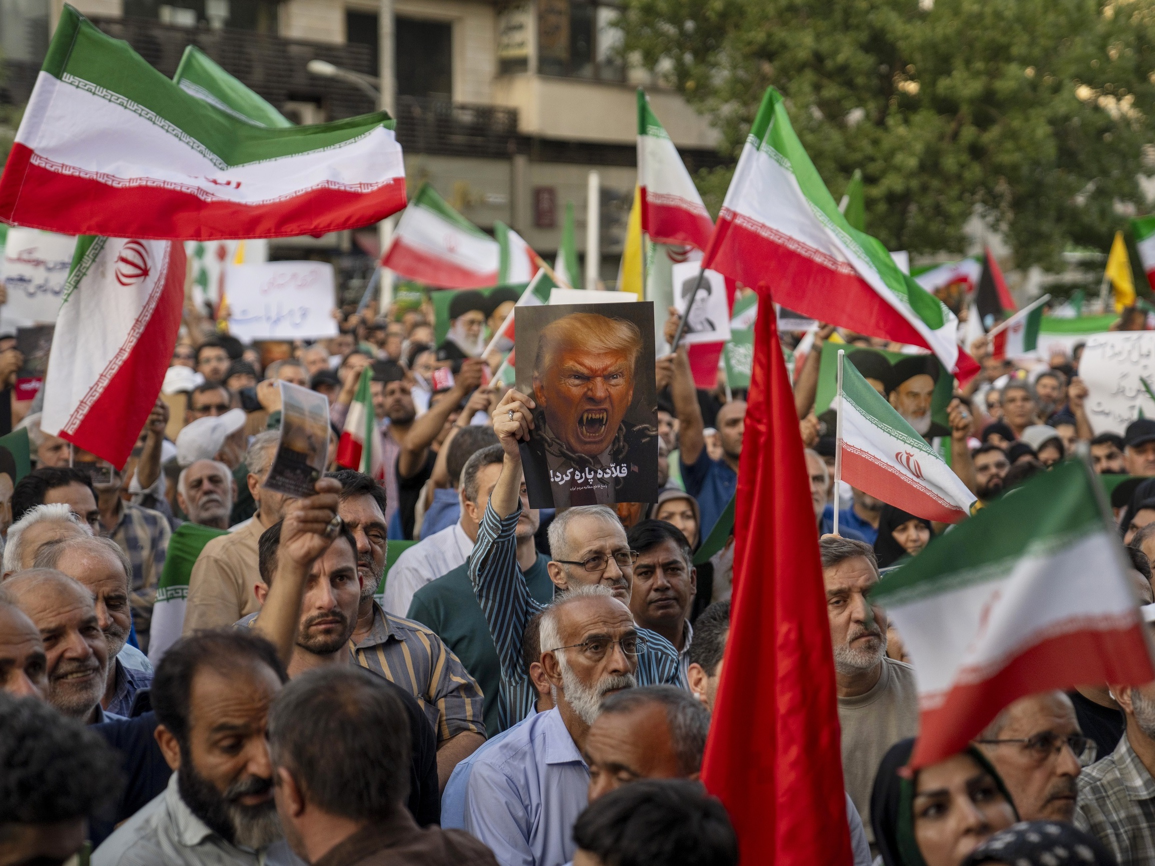 caption: Iranian protesters chant slogans and one holds a poster with a vampire-like illustration of President Trump in Tehran's Revolution Square on Sunday to protest the U.S. attacks on nuclear sites in Iran.