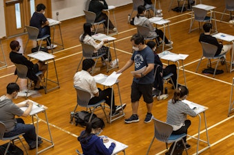 caption: An invigilator distributes papers to students taking the Hong Kong Diploma of Secondary Education exams on April 22, in Hong Kong.