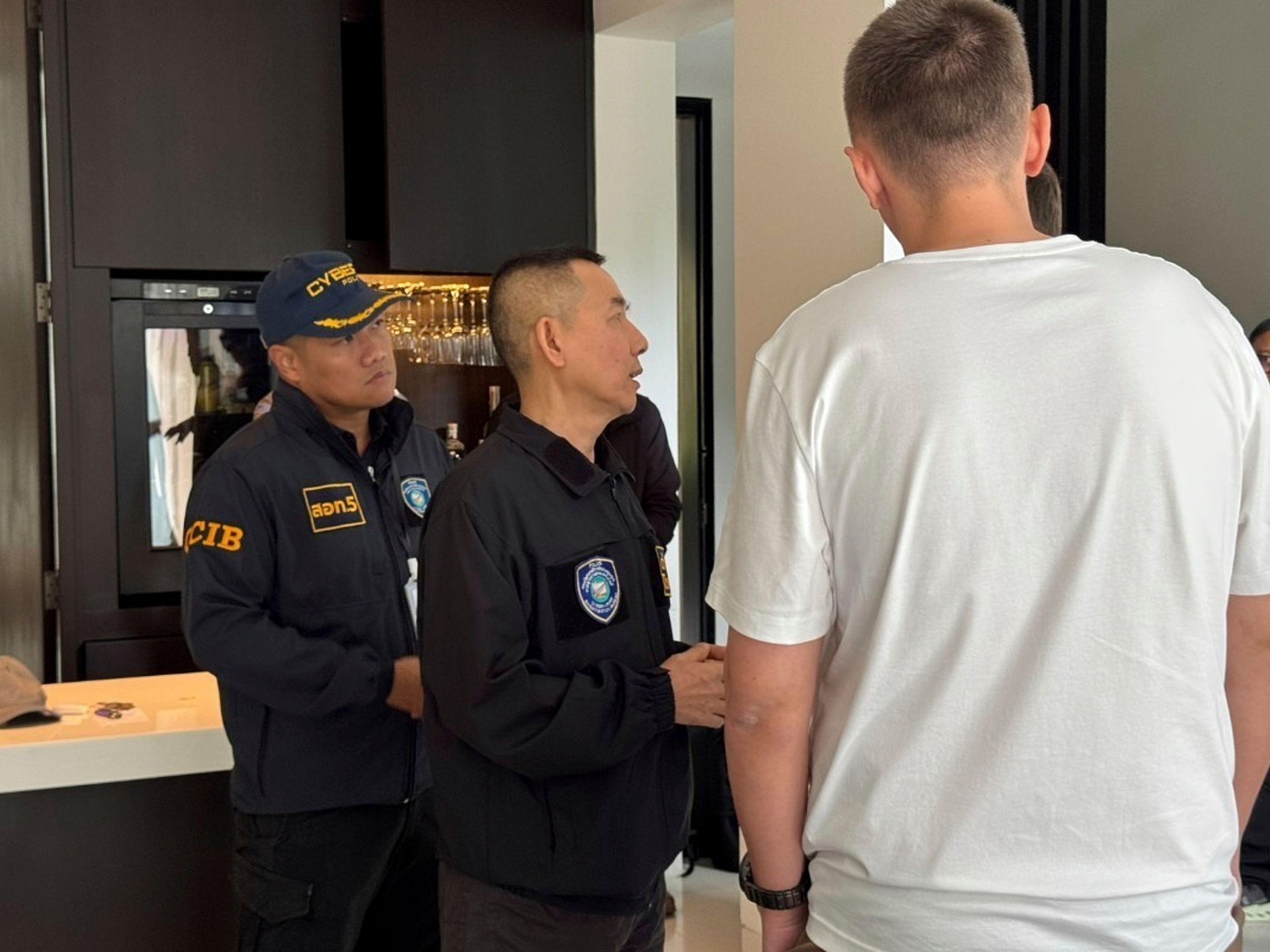 caption: A 35-year-old suspected Russian hacker, identified in Russian media as Denis Obrezko, right, back to camera, with cyber police after he was arrested in Phuket, Thailand on Nov. 6. 2025.