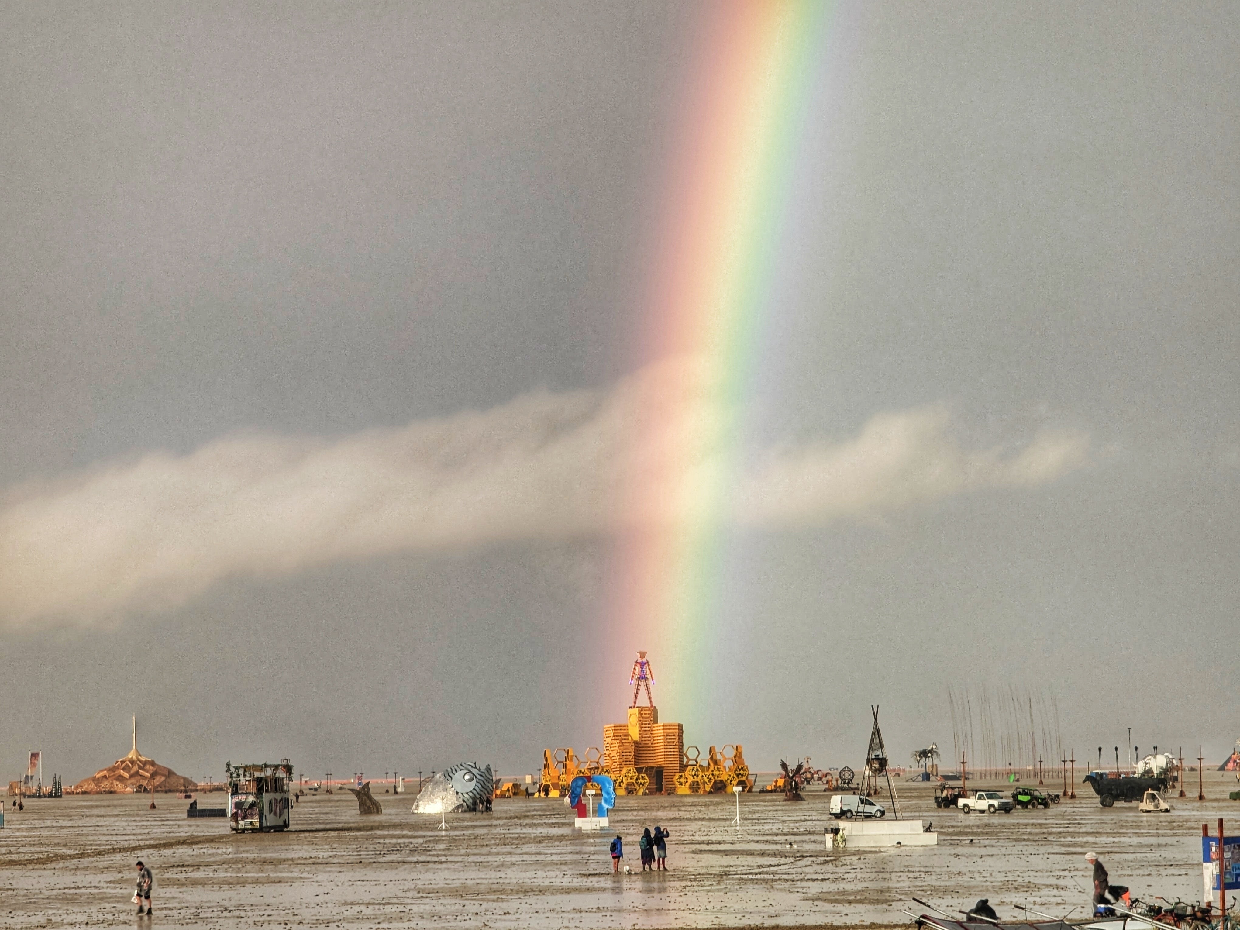 caption: Burning Man attendee Josh Lease climbed on top of his camp's trailer to take a photo of the rainbow that emerged after heavy rains brought muddy grounds at the Black Rock City playa on Saturday.