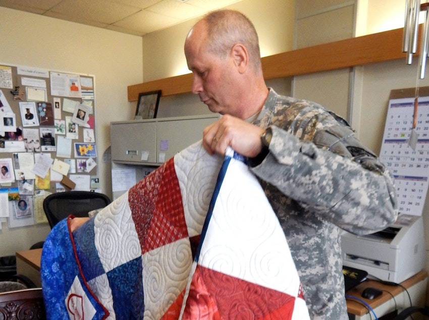 caption: Col. Kenneth Trzepkowski, chief of palliative care at Madigan Army Medical Center, unfolds one of the handmade quilts donated to the hospital for the palliative care patients.