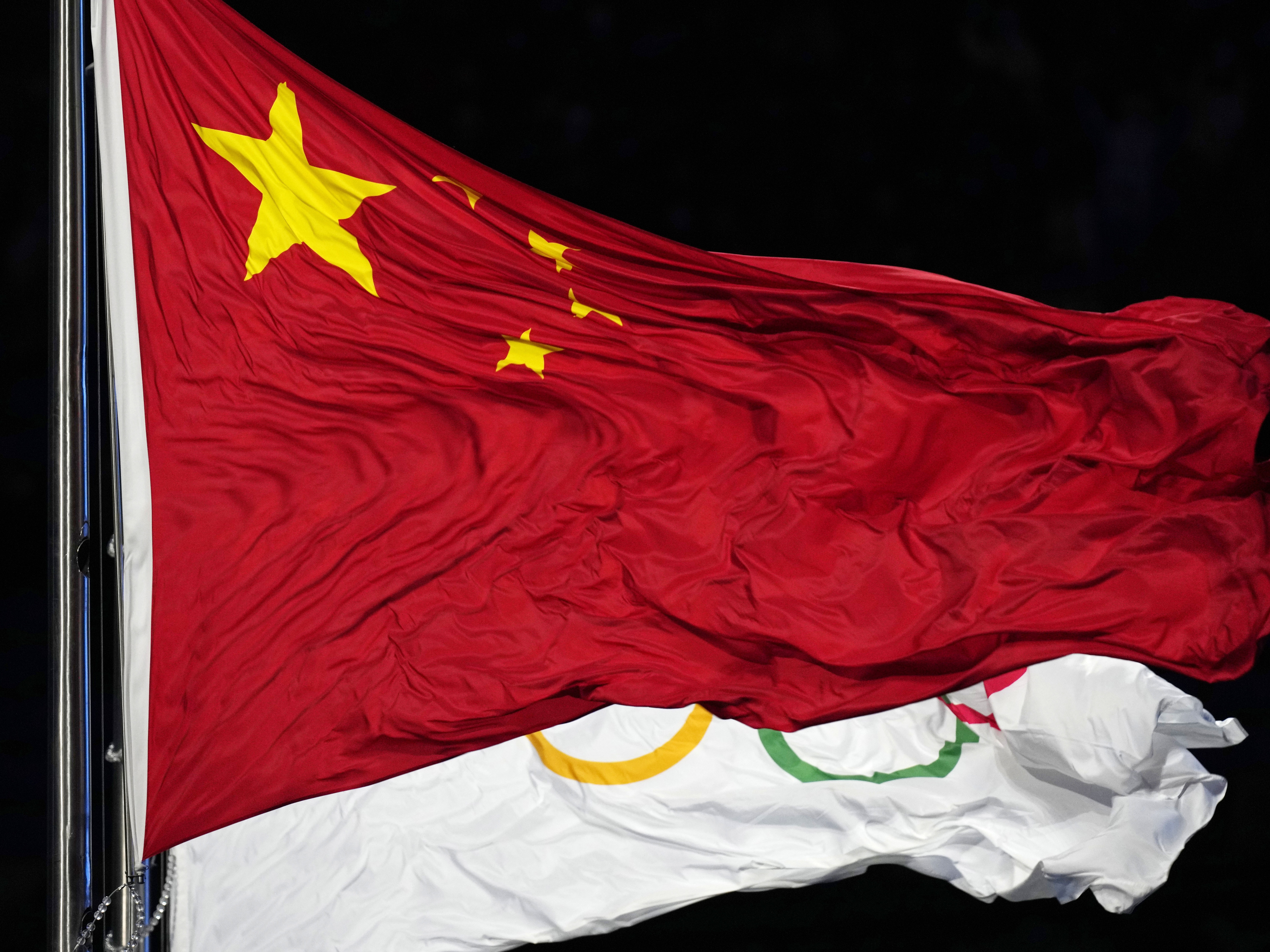 caption: The Chinese and the Olympic flag wave during the opening ceremony of the 2022 Winter Olympics in Beijing. The World Anti-Doping Agency cleared 23 Chinese swimmers of doping allegations despite positive tests for banned substances, allowing them to compete in the 2021 Tokyo Games.