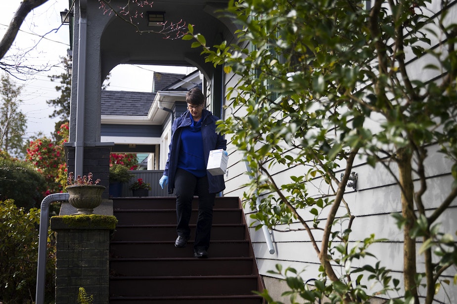 caption: Dawn Lum, with the Seattle Mask Brigade, collects a donated box of masks from a porch on Wednesday, April 1, 2020, in Seattle. 