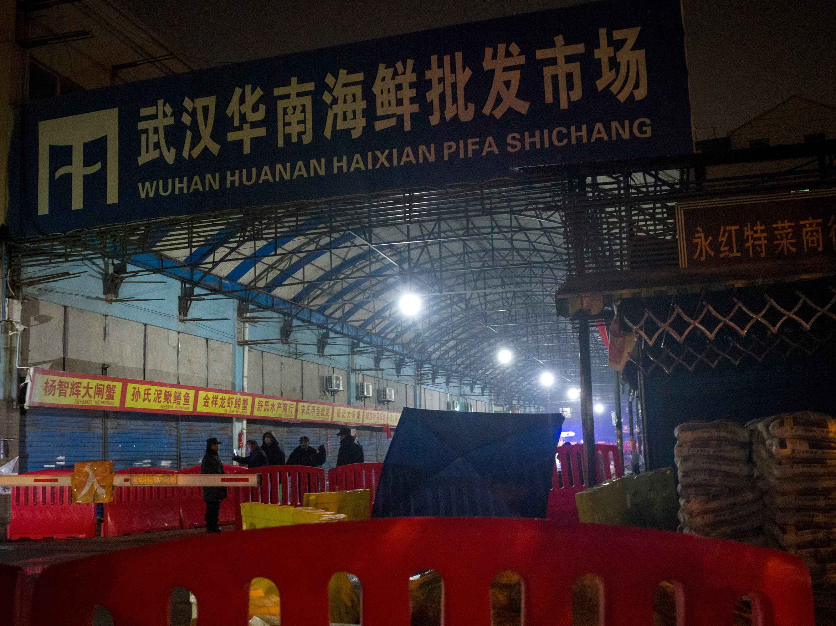 caption: Security guards stand in front of the Huanan Seafood Wholesale Market in Wuhan, China, on Jan. 11, 2020, after the market had been closed following an outbreak of COVID-19 there. Two studies document samples of SARS-CoV-2 from stalls where live animals were sold.