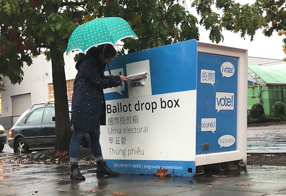 caption: A King County voter submits their ballot at a ballot drop box in Seattle's Lake City neighborhood. 