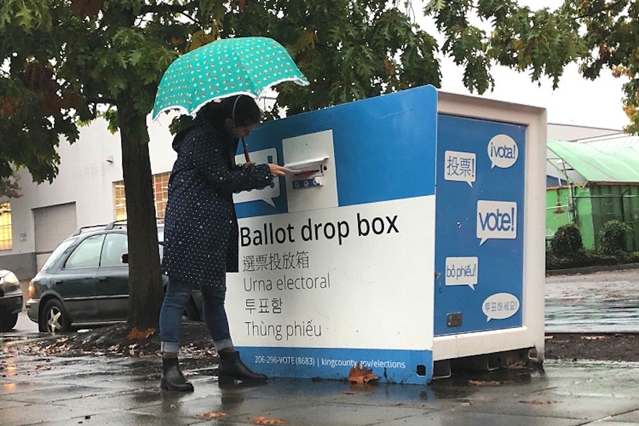 caption: A King County voter submits their ballot at a ballot drop box in Seattle's Lake City neighborhood. 