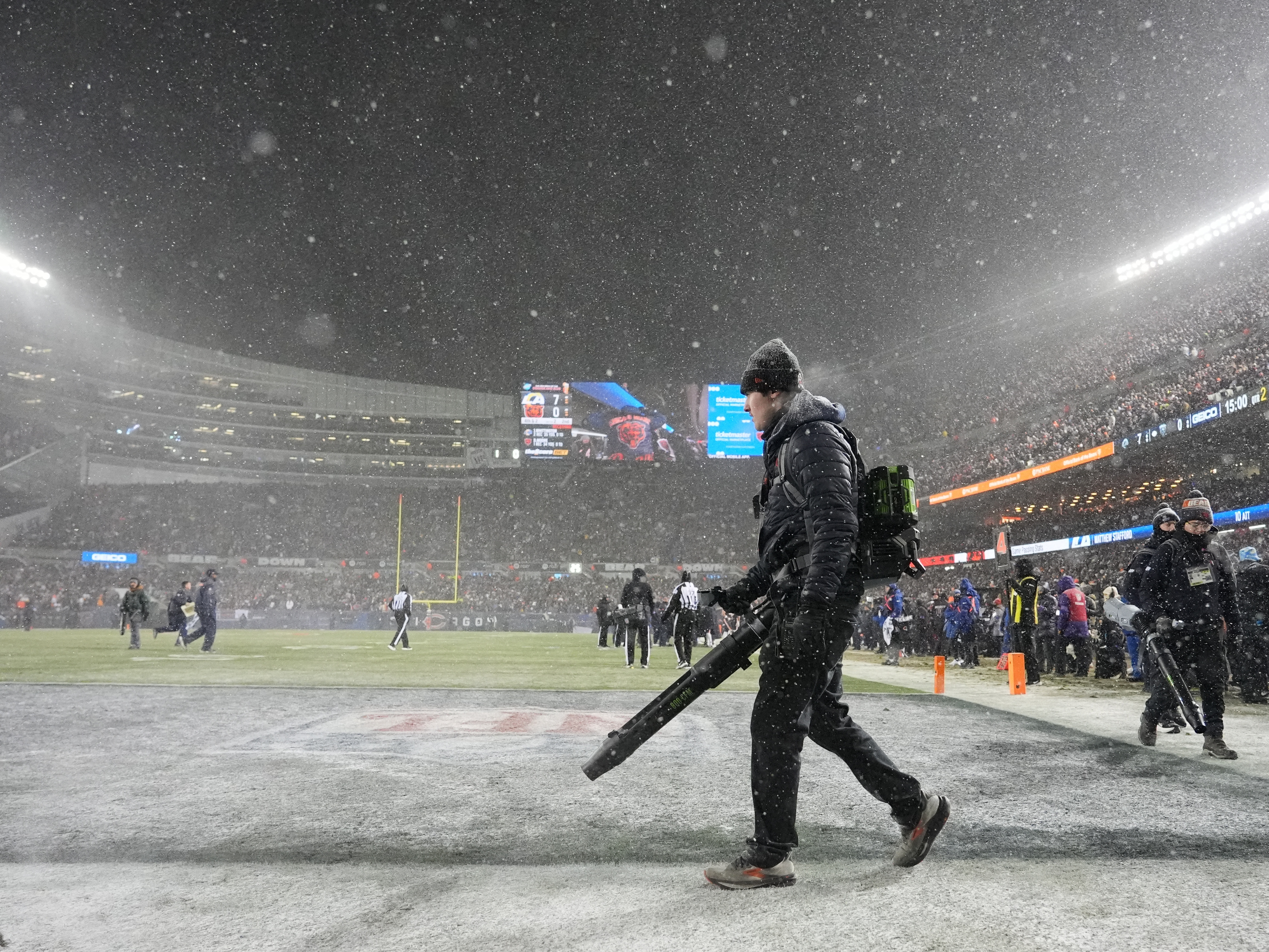 caption: Grounds crew members glow snow off the field at Soldier Field during the first half of an NFL football divisional playoff game between the Chicago Bears and the Los Angeles Rams Sunday, Jan. 18, 2026, in Chicago.