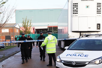 caption: Essex police officers at the scene where 39 bodies were found in the back of a truck on October 24.