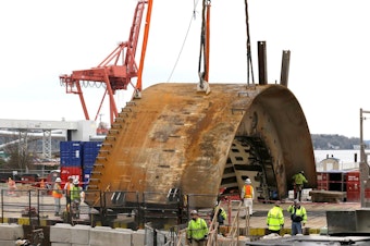 caption: One section of Bertha's front body now sits on the ground near the rescue pit.