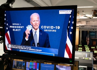 caption: President-elect Joe Biden is shown speaking on a monitor about COVID-19 in the briefing room of the White House on November 9, 2020, in Washington, D.C. (Joshua Roberts/Getty Images)