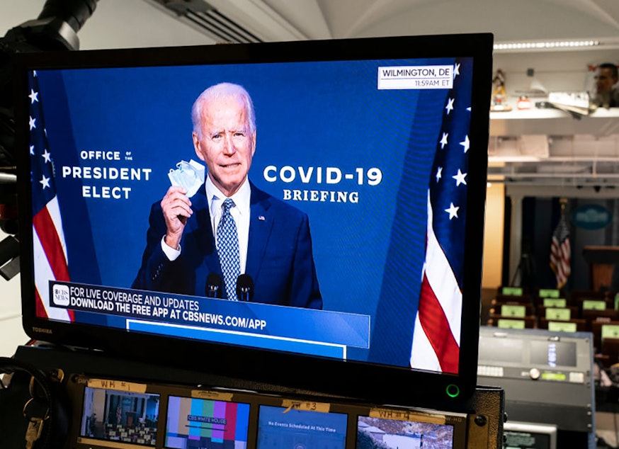 caption: President-elect Joe Biden is shown speaking on a monitor about COVID-19 in the briefing room of the White House on November 9, 2020, in Washington, D.C. (Joshua Roberts/Getty Images)