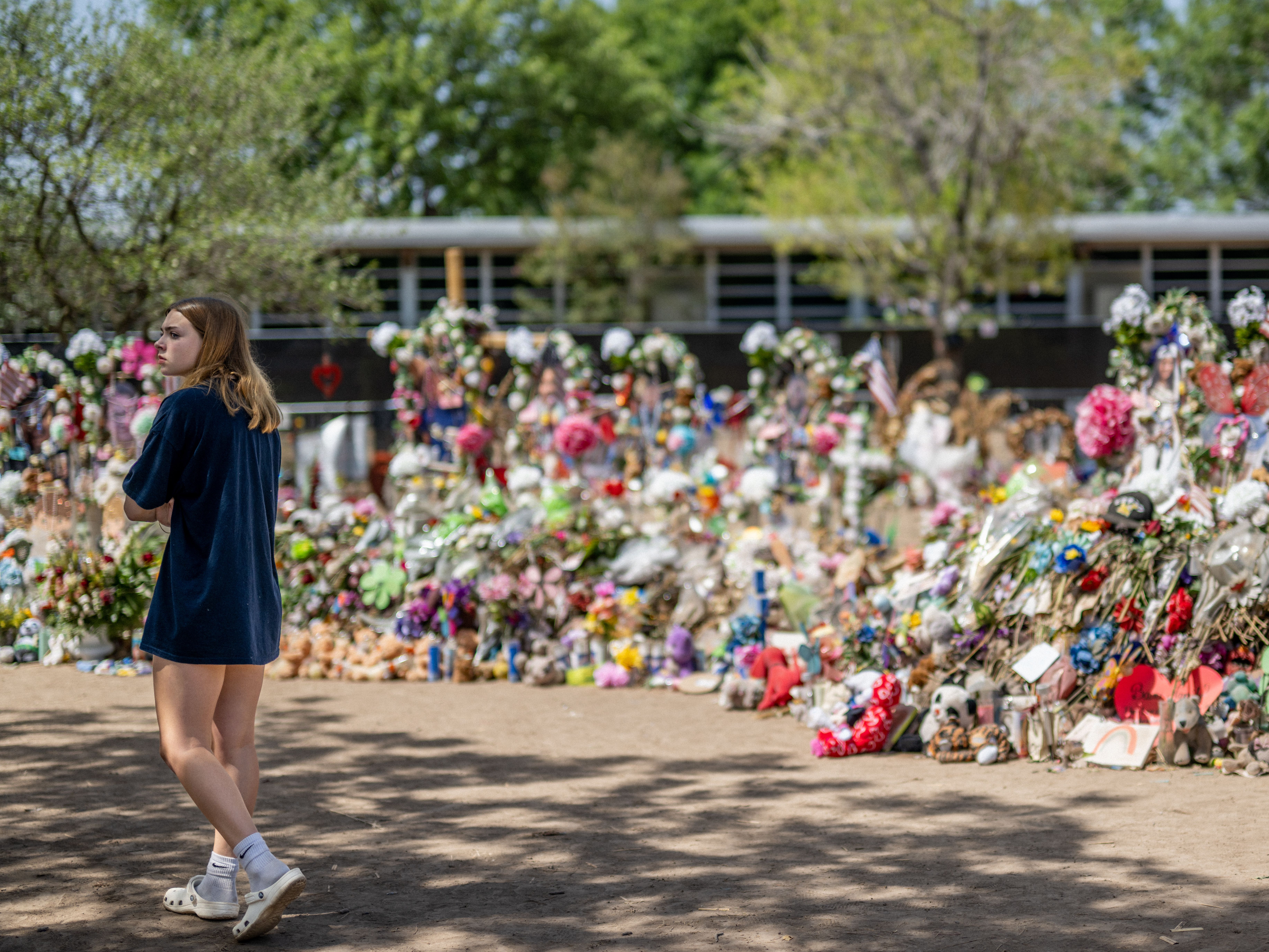 caption: A young woman pays her respects at a memorial in front of Robb Elementary School earlier this monthin Uvalde, Texas. Committees have begun inviting testimony from law enforcement authorities, family members and witnesses regarding the mass shooting at Robb Elementary School which killed 19 children and two adults.
