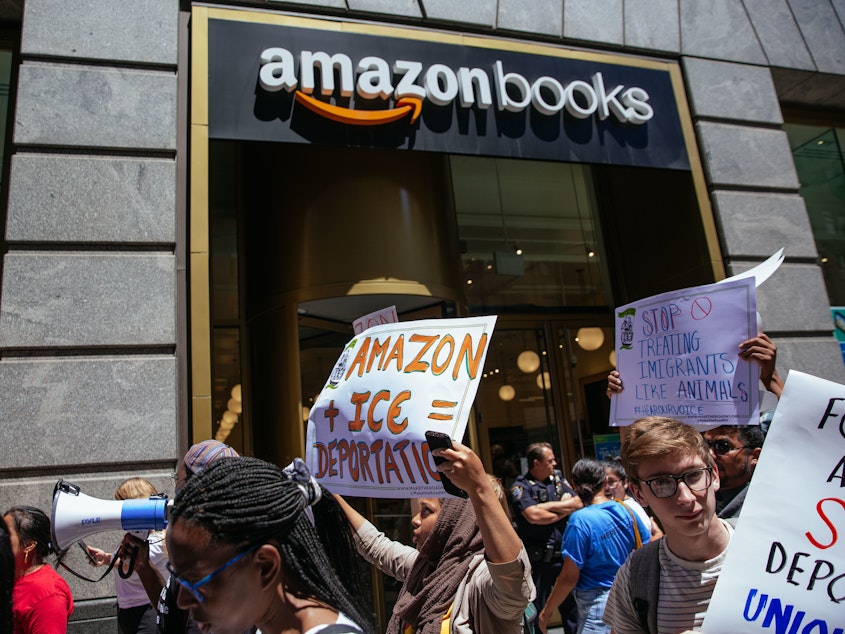 caption: Protesters march to an Amazon store to raise awareness of Amazon facilitating ICE surveillance efforts.