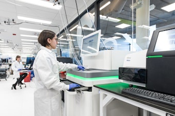 caption: An employee of the Boston biotech company Ginkgo Bioworks runs a gene sequencing machine through its paces. The company synthesizes thousands of genes a month, which are then inserted into cells that become mini factories of useful products.