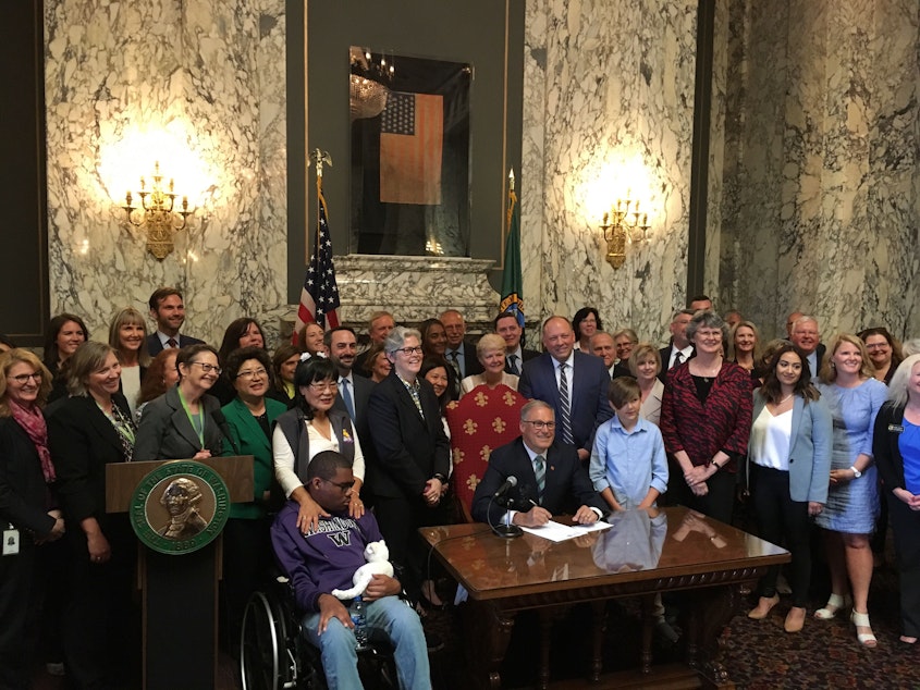 caption: Wash. Gov. Jay Inslee poses for a photo after signing the state's new health care law on May 5, which would create a public health care plan available to people of any income level. He also signed a law creating a new long-term care plan.